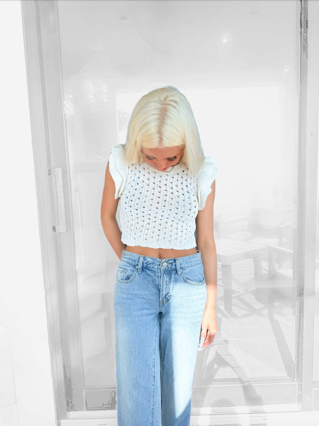 White open-knit cropped top with ruffle sleeves, modeled against a blurred background.
