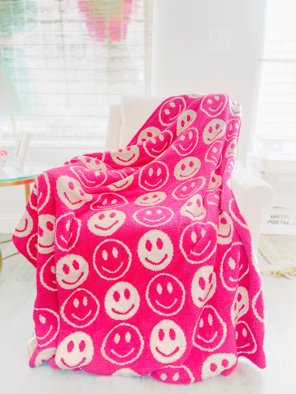 Pink fuzzy blanket draped over a chair, featuring a cheerful smiley face pattern.
