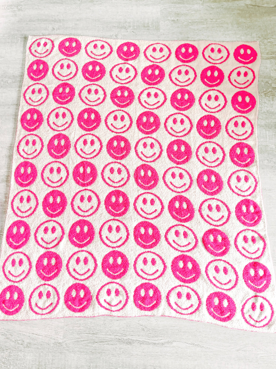 Soft pink and white plush blanket adorned with cheerful smiley faces.
