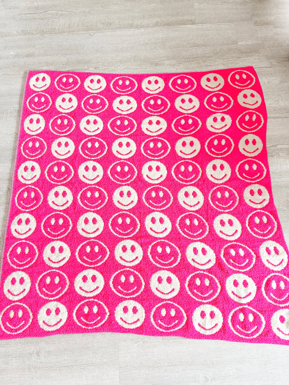 Pink fuzzy blanket with repeating smiling face pattern.
