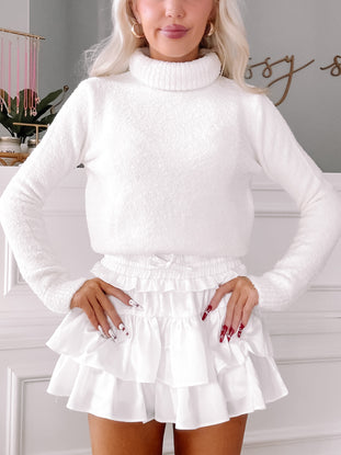 White fluffy turtleneck sweater styled with a white ruffled mini skirt.
