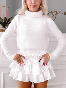 White fluffy turtleneck sweater styled with a white ruffled mini skirt.
