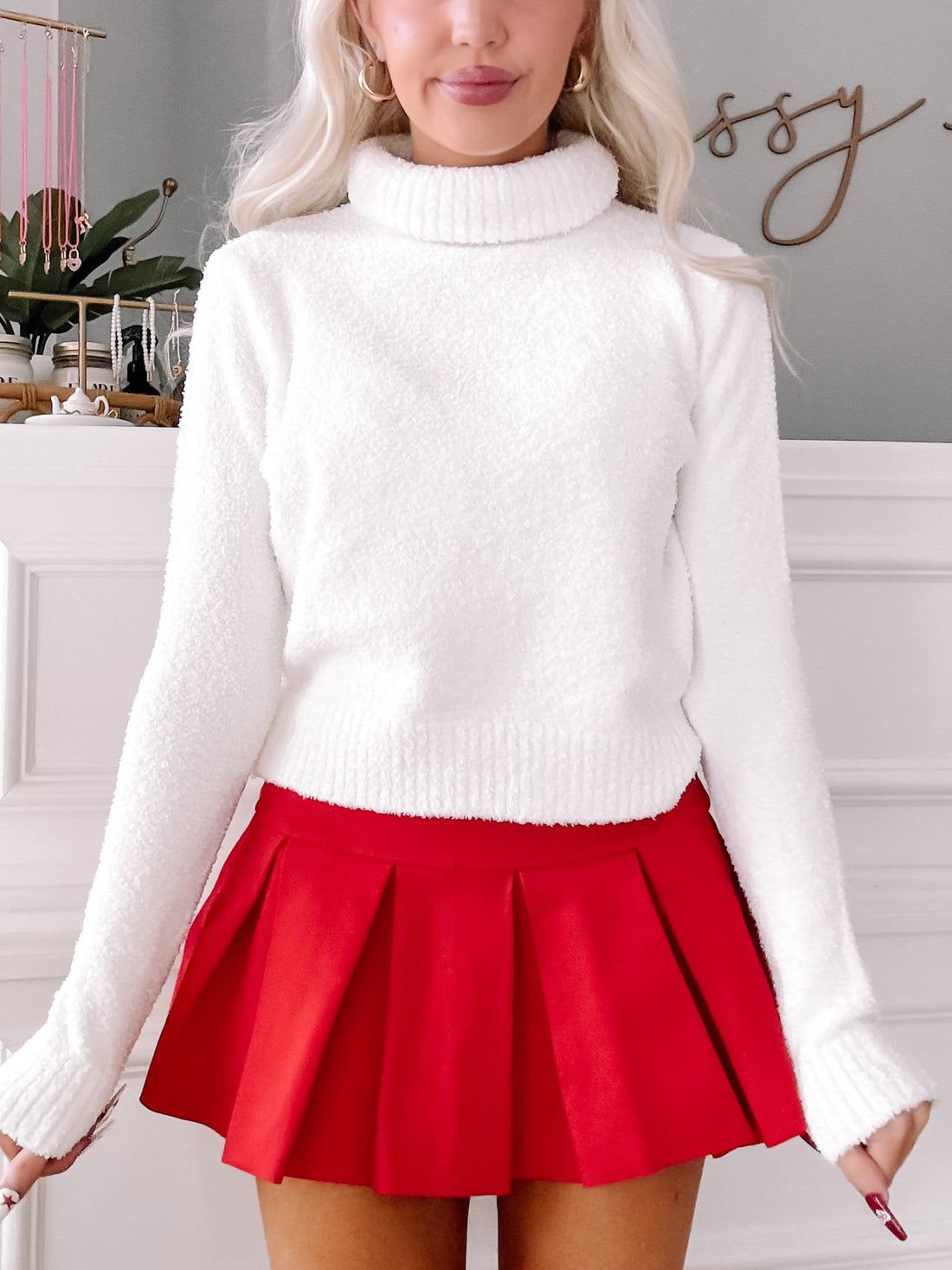 White fuzzy turtleneck sweater paired with a red pleated mini skirt.

