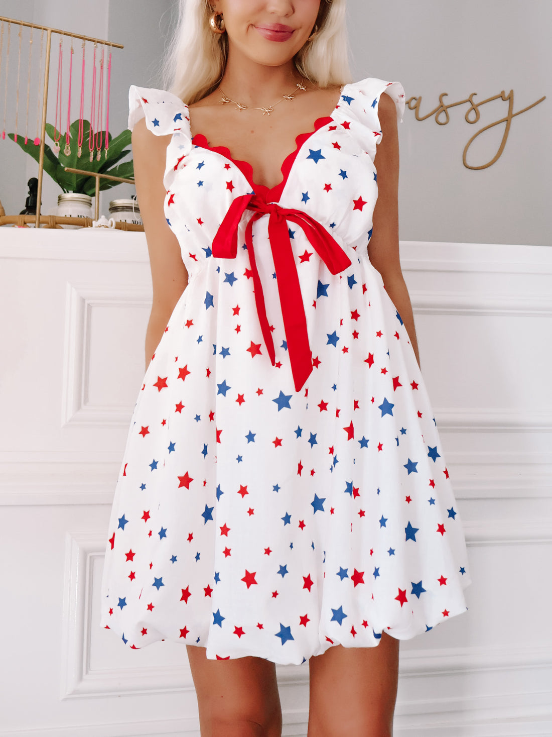 Model wearing white babydoll dress with red bow and blue star print, perfect for July Fourth.