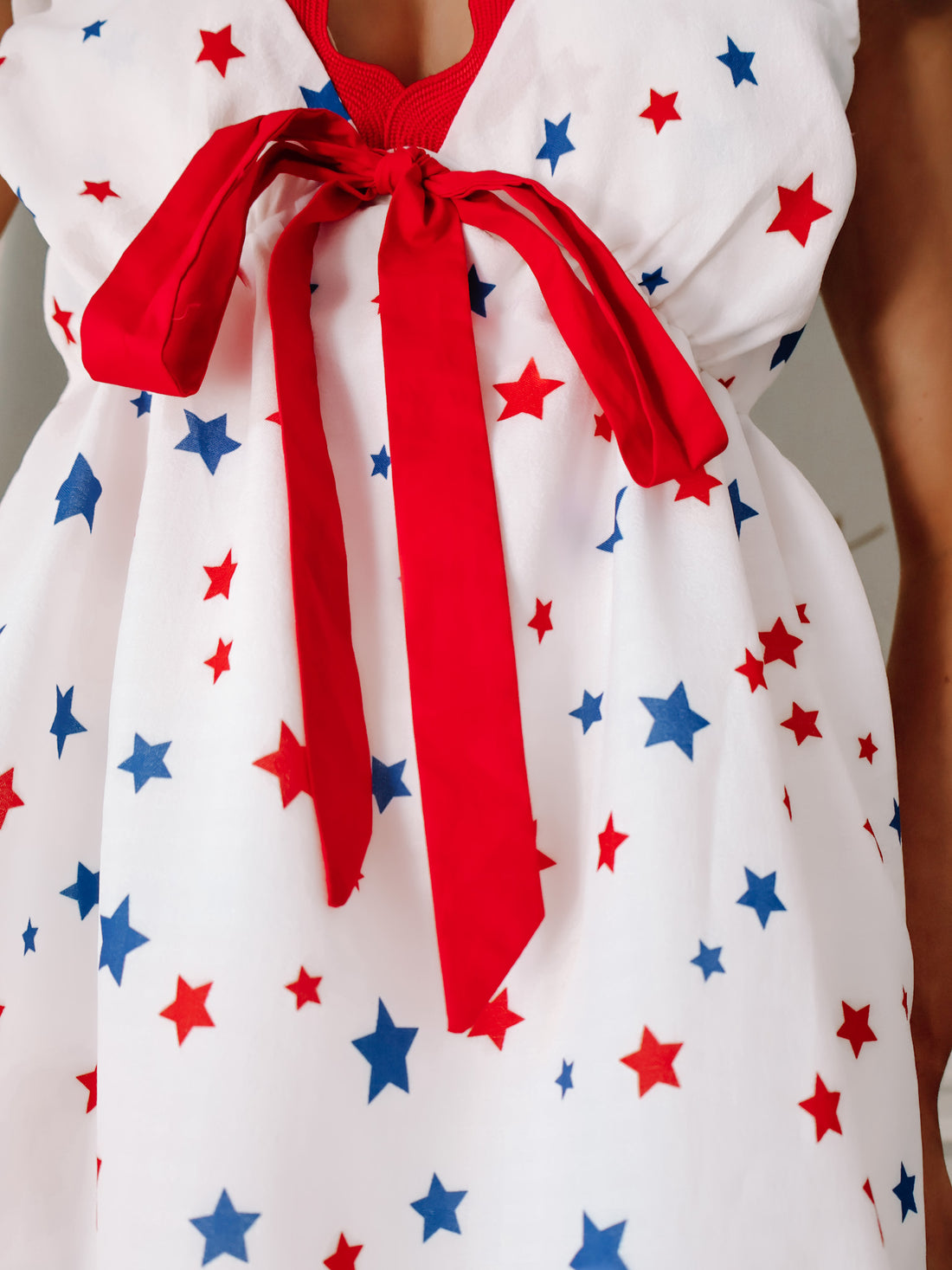 Close-up of red bow detail and star print on Sassy Shortcake’s patriotic babydoll dress.