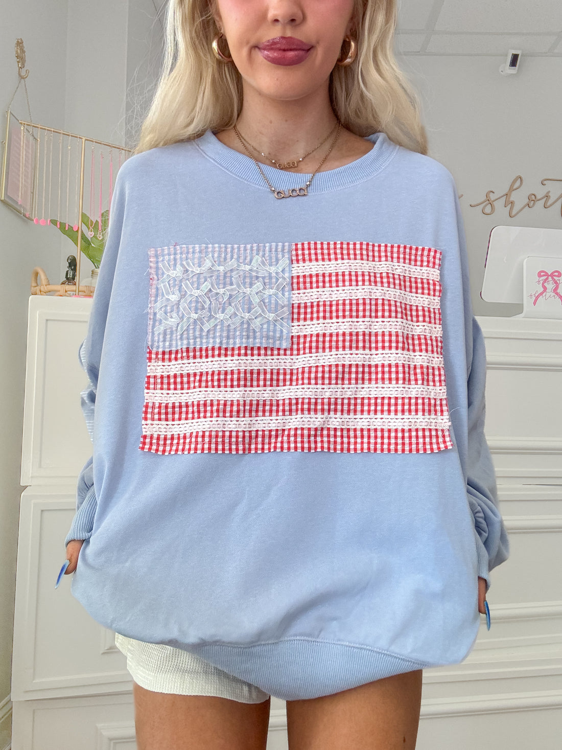 Close-up of patchwork flag and bow accents on blue sweatshirt.