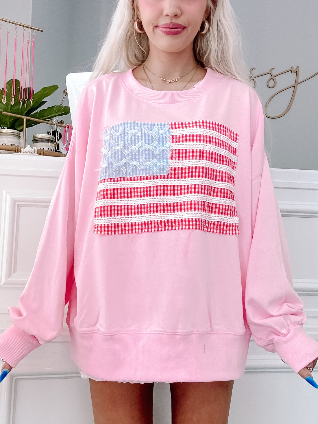 Model wearing pink oversized crewneck with American flag patchwork and bow accents.