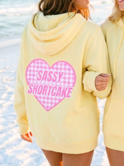 Sun Love Zip Up from Sassy Shortcake - Person wearing a yellow hoodie with 'Sassy Shortcake' on a beach