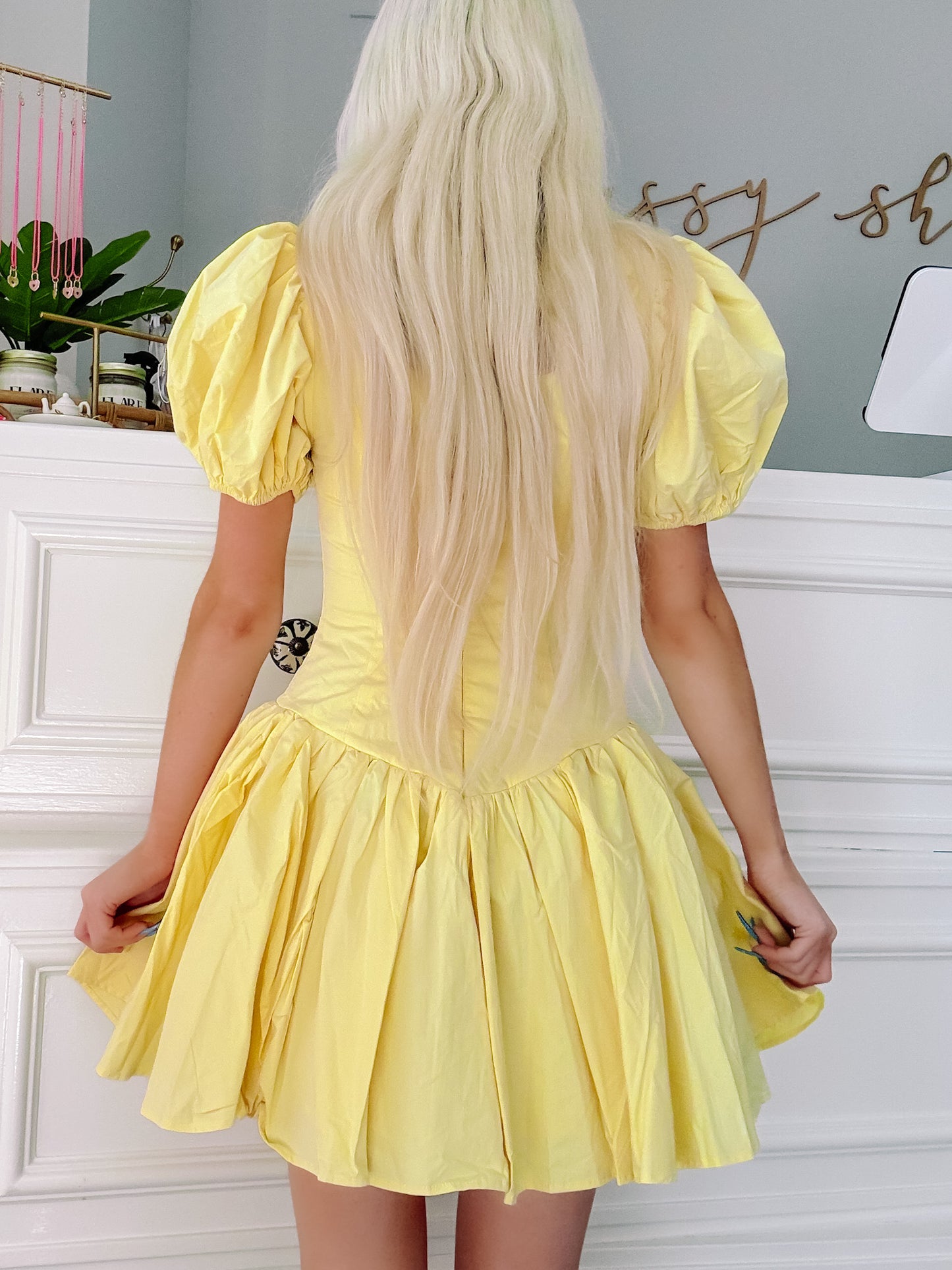 Pale yellow puff-sleeve mini dress, shown from behind against a white wall.
