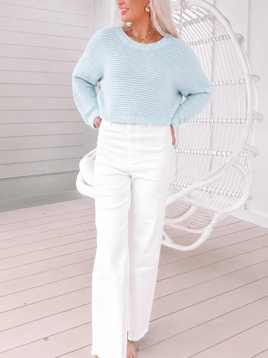 Woman wearing a pastel light blue Sassy Shortcake Almond Sweater showing the detailed round neckline and ribbed cuffs with white pants 