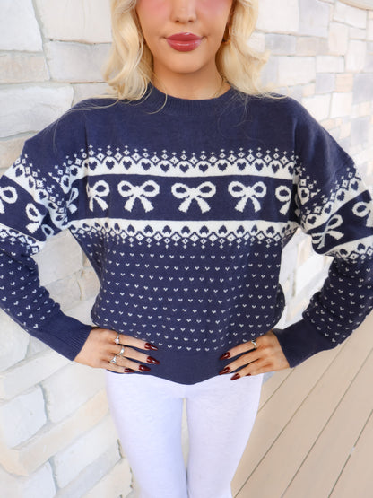 Close-up of the navy sweater showing the large white graphic design of a bow and hearts on the soft knit fabric.