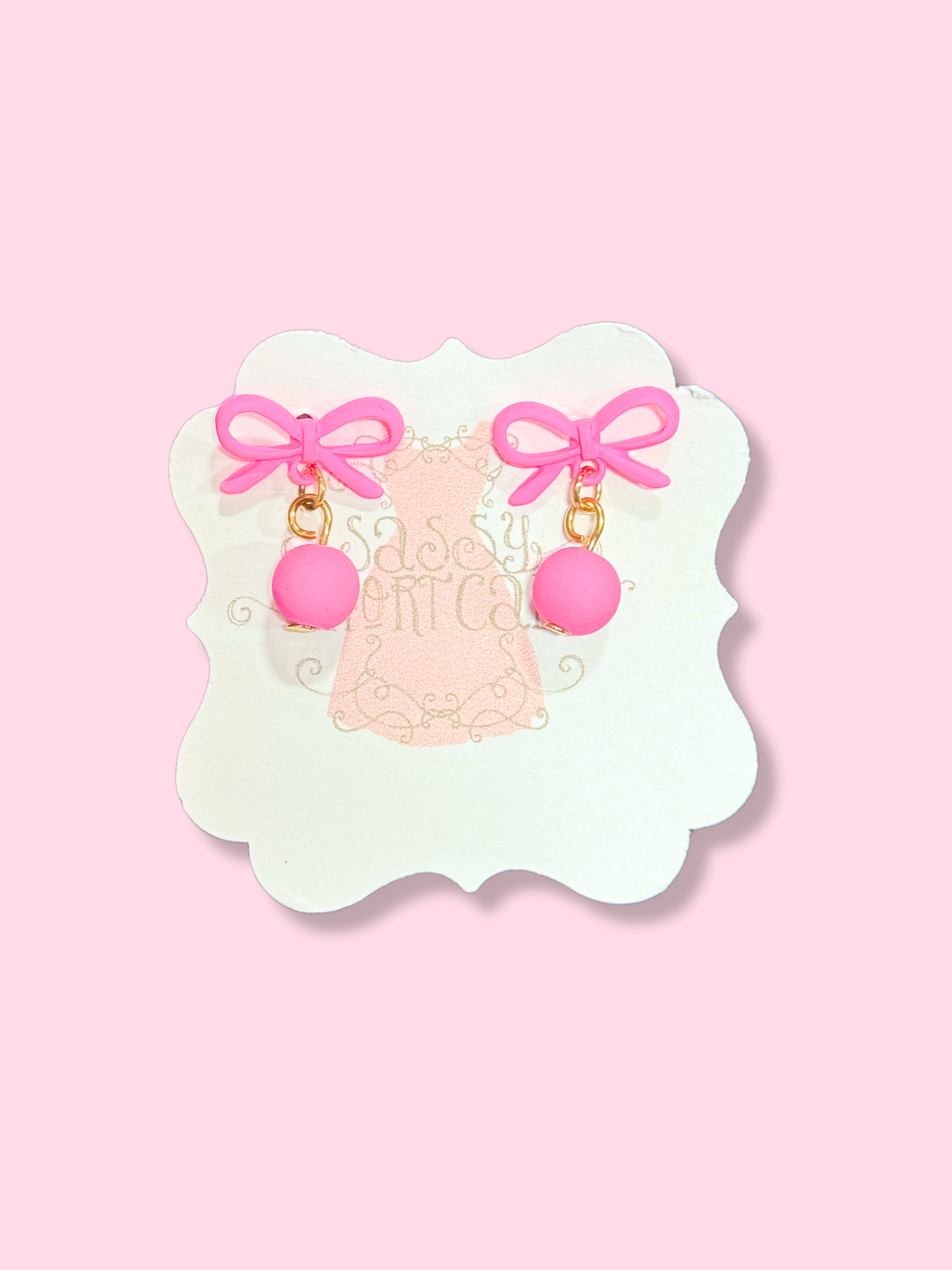 Amara Bow Earrings: Pink matte ball & bow earrings on white display card
