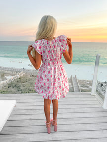 Pink floral dress viewed from behind, on a deck overlooking the ocean at sunset.
