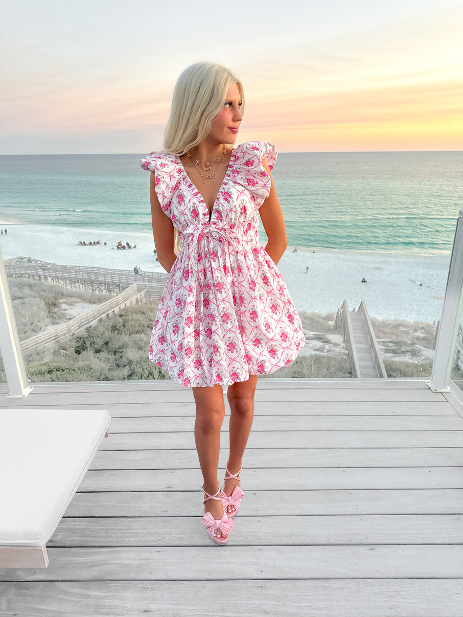 Pink floral mini dress worn on a beachside deck at sunset.
