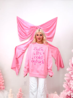 Model wearing a pink crewneck sweatshirt with the text "Baby It's Cold Outside" and snowflakes in hot pink, showing the fleece lining detail.
