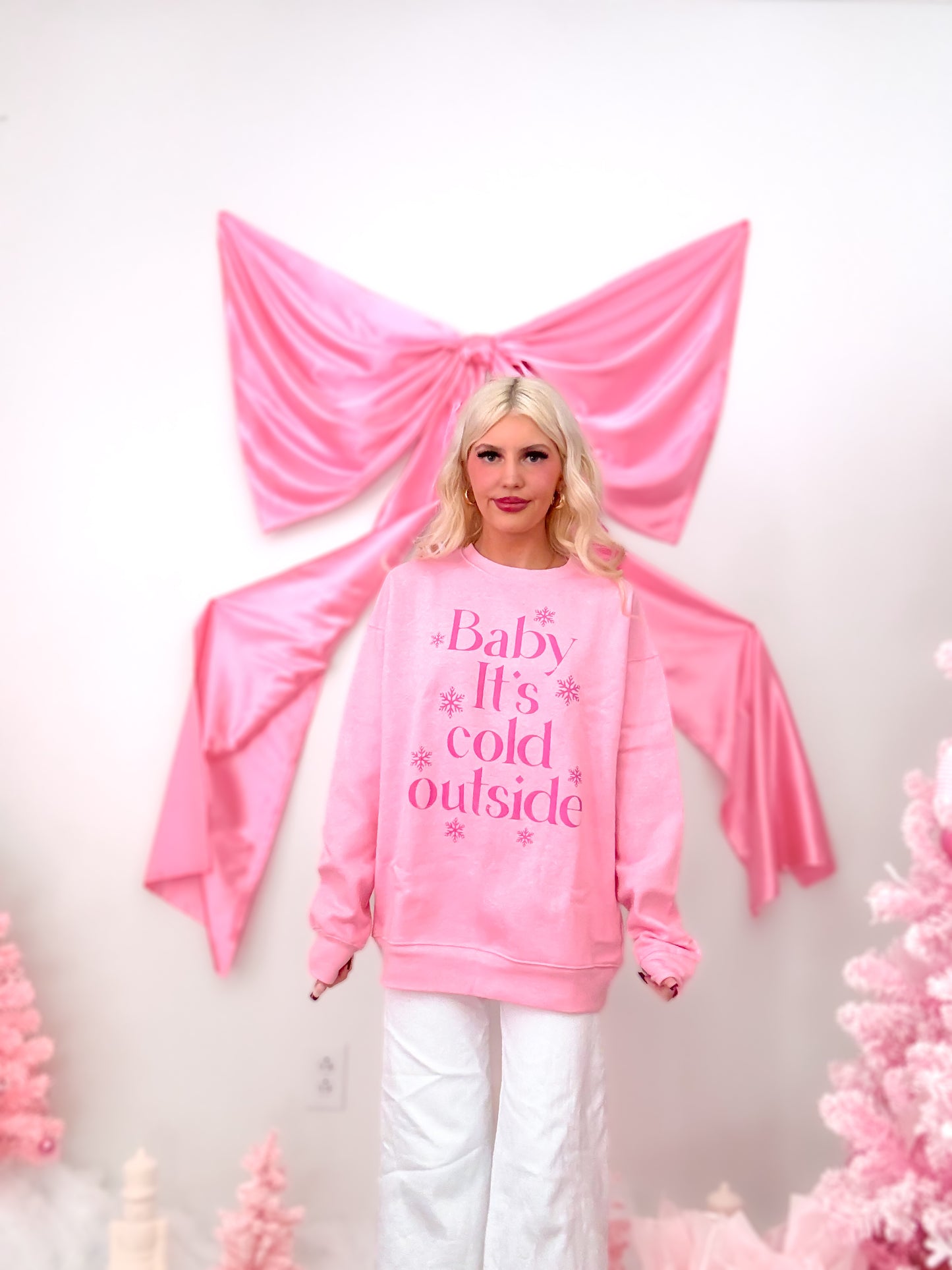 Model wearing a pink crewneck sweatshirt with the text "Baby It's Cold Outside" and snowflakes in hot pink, showing the fleece lining detail.