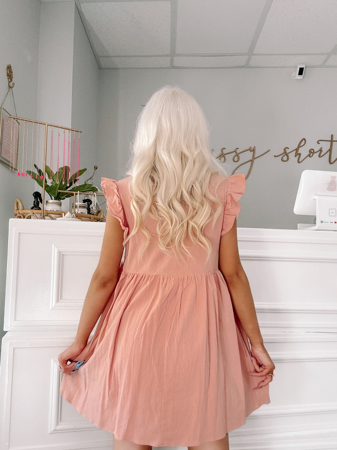 Dusty rose mini dress with ruffle sleeves, shown from the back in a boutique setting.
