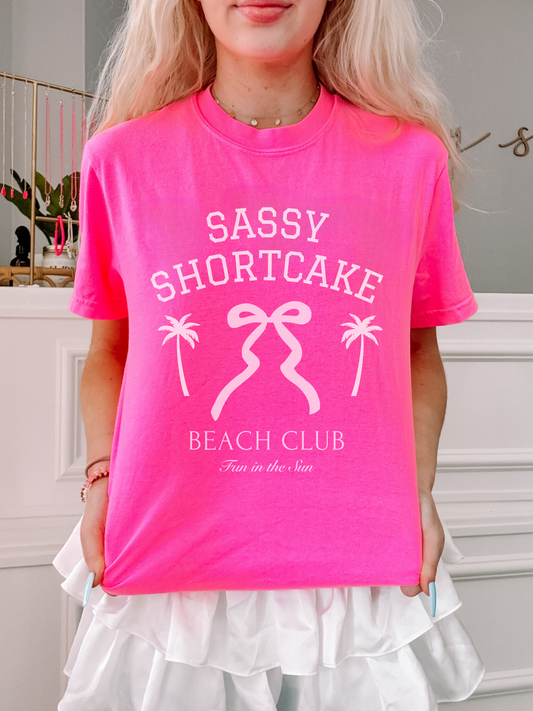Front view of a model in the pink Sassy Shortcake tee featuring a white bow logo, posed on white background.