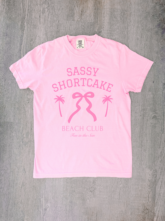 Flatlay of soft pink tee featuring bow logo, shot from above.