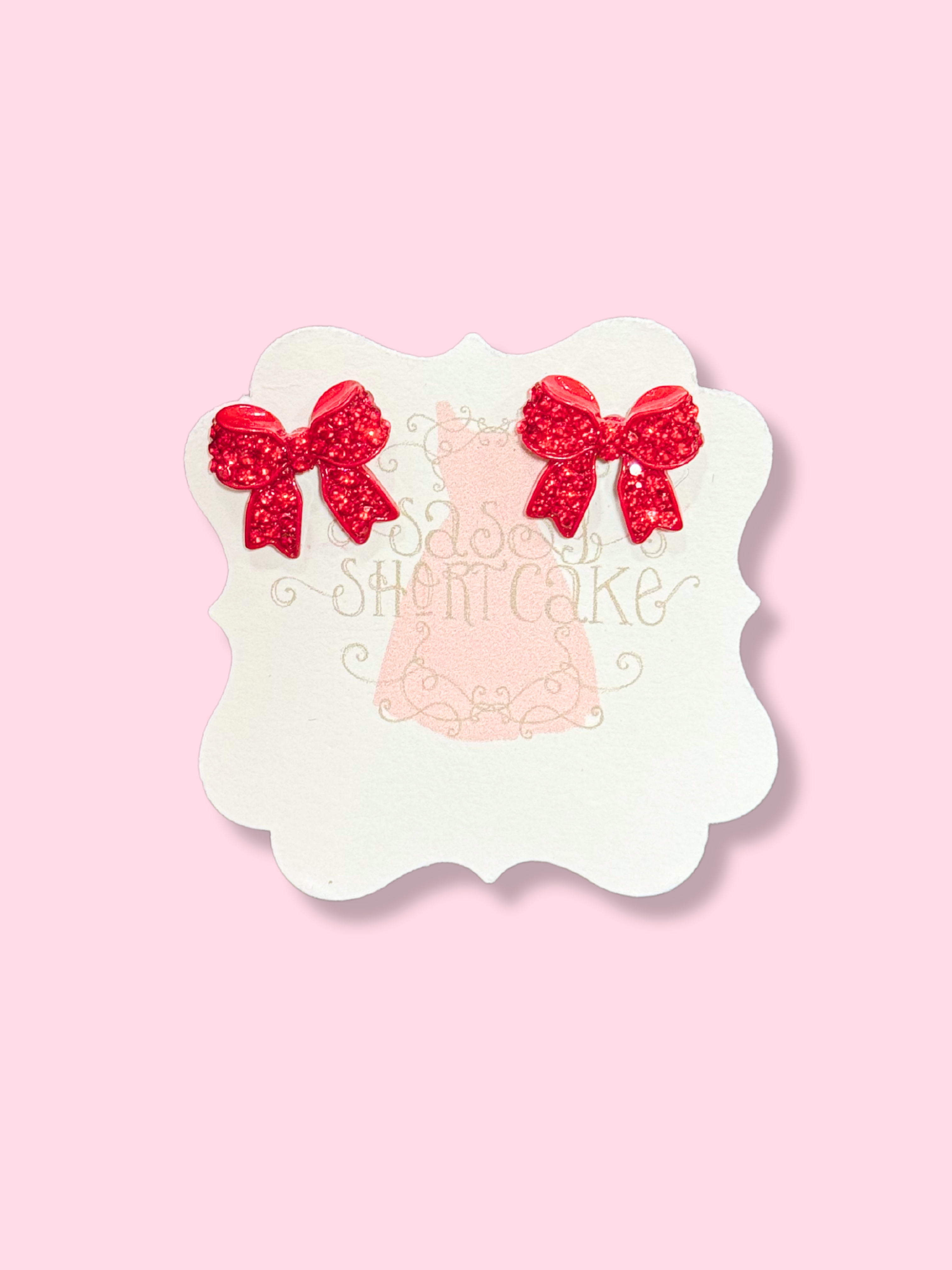 Red bedazzled bow earrings on pink background
