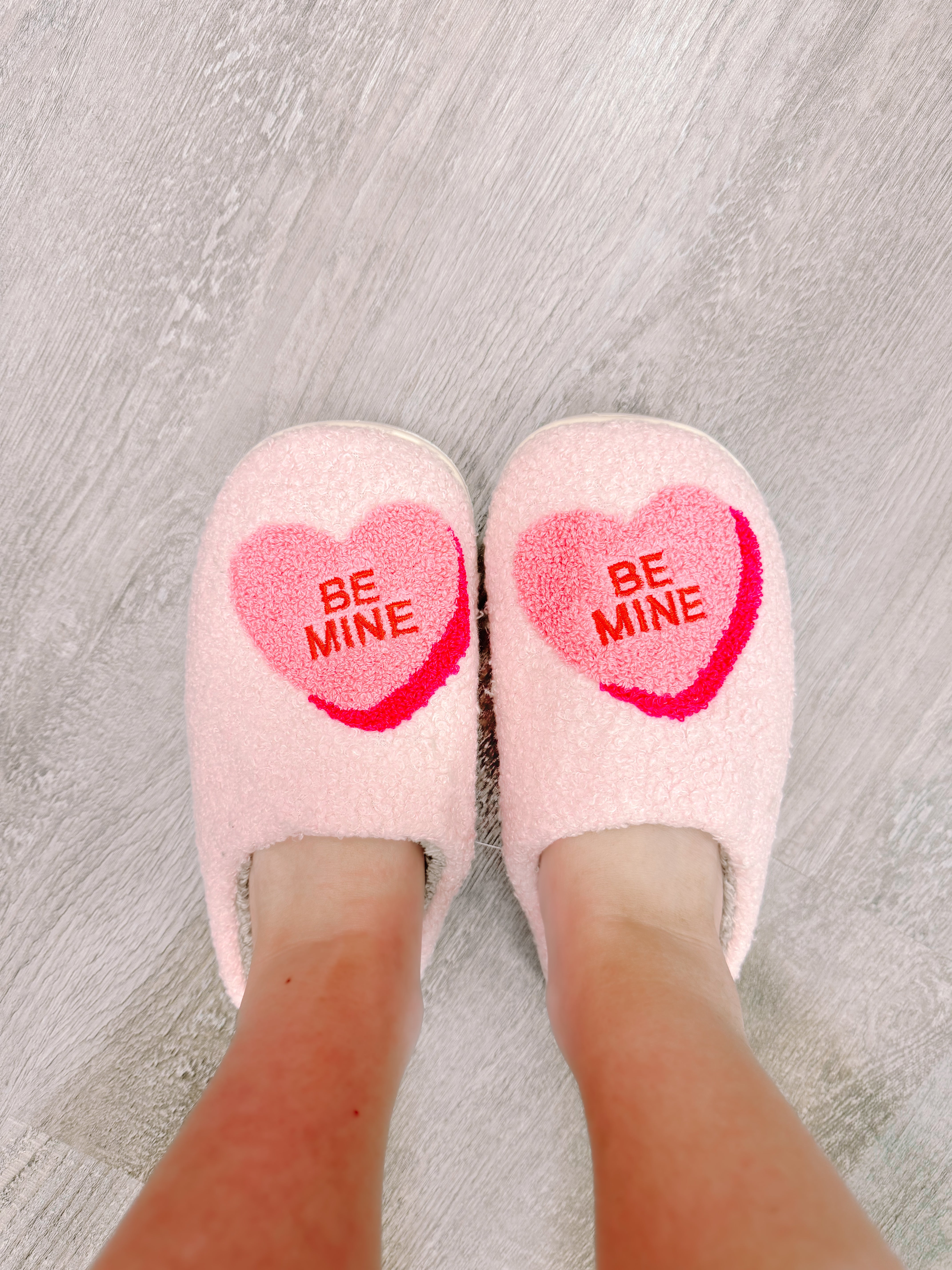 Pink fuzzy slippers with heart design reading 