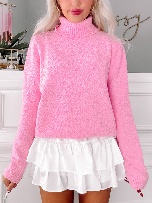 Pink fuzzy turtleneck sweater styled with a white ruffled skirt.