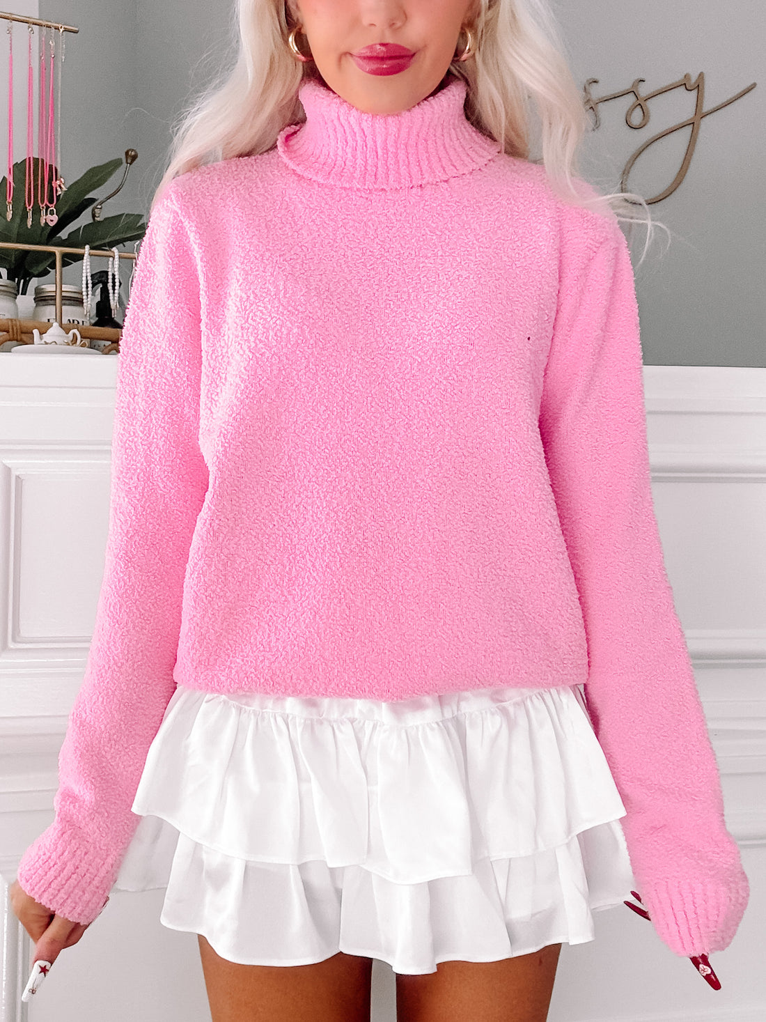 Pink fuzzy turtleneck sweater styled with a white ruffled skirt.
