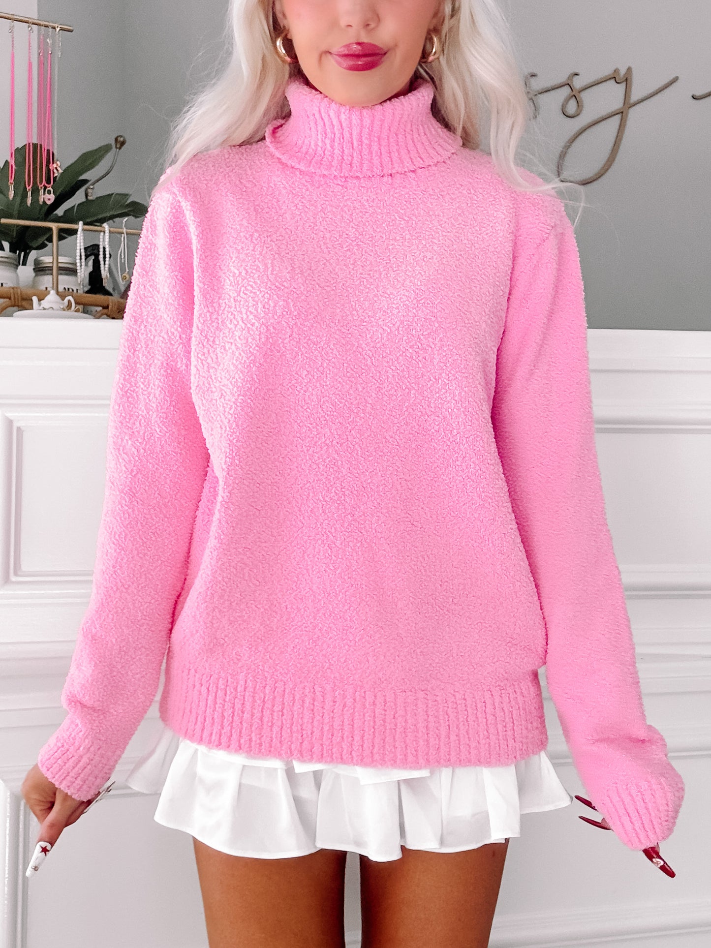 Pink fuzzy turtleneck sweater styled with a white pleated skirt.
