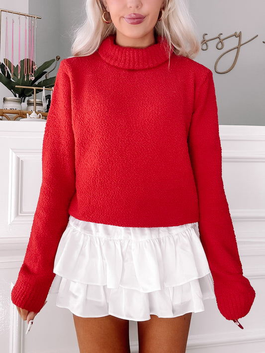Red textured turtleneck sweater paired with a white ruffled mini skirt.