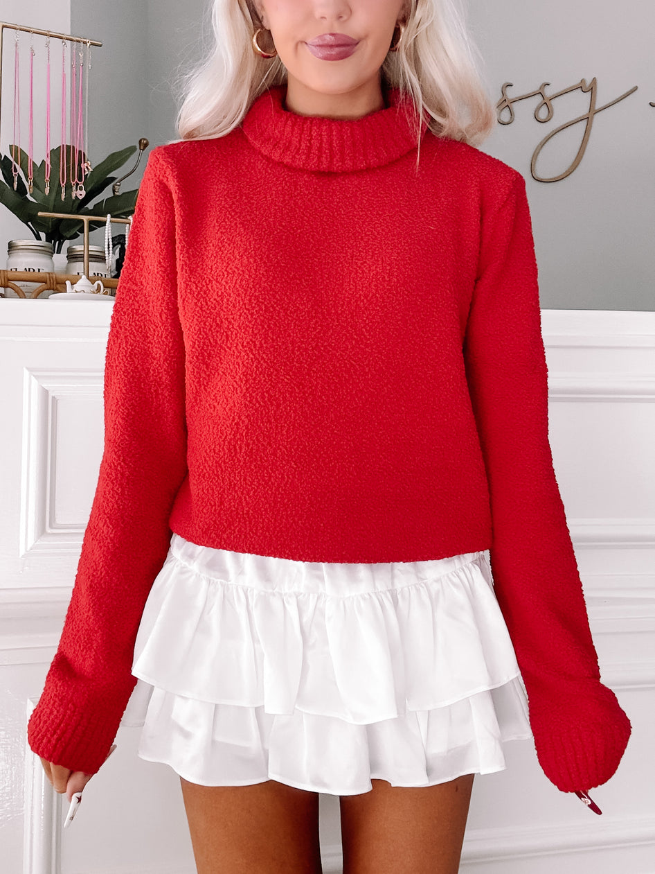 Red textured turtleneck sweater paired with a white ruffled mini skirt.
