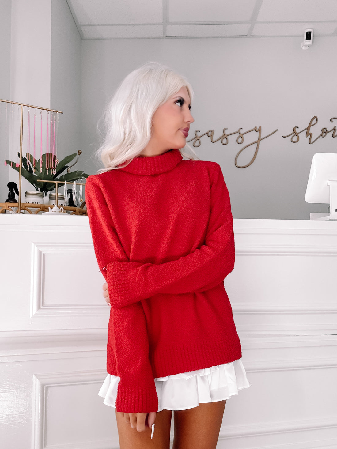 Red turtleneck sweater styled with a white ruffled skirt, in a shop setting.
