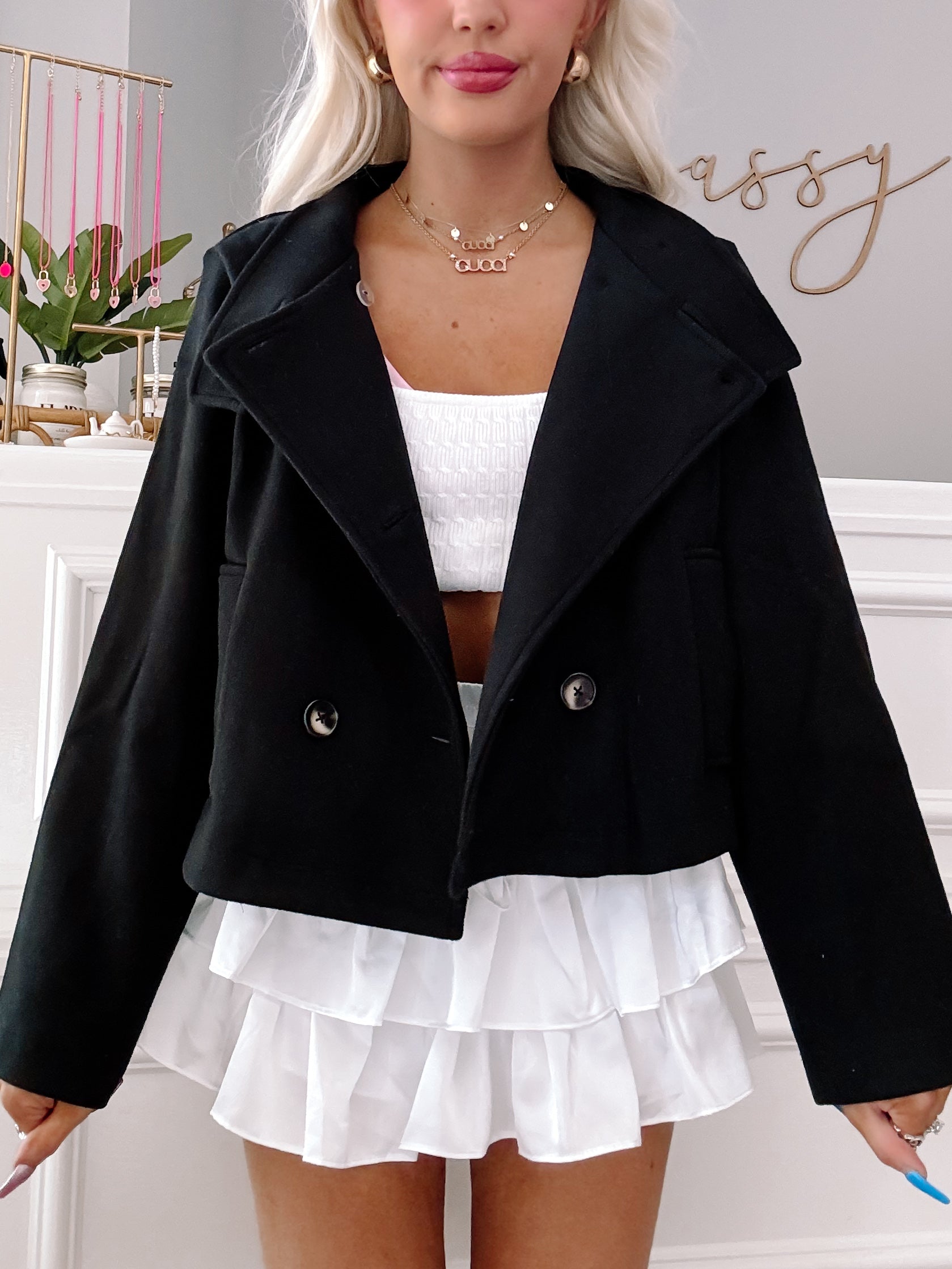 Black cropped double-breasted jacket styled with a white ruffled skirt.
