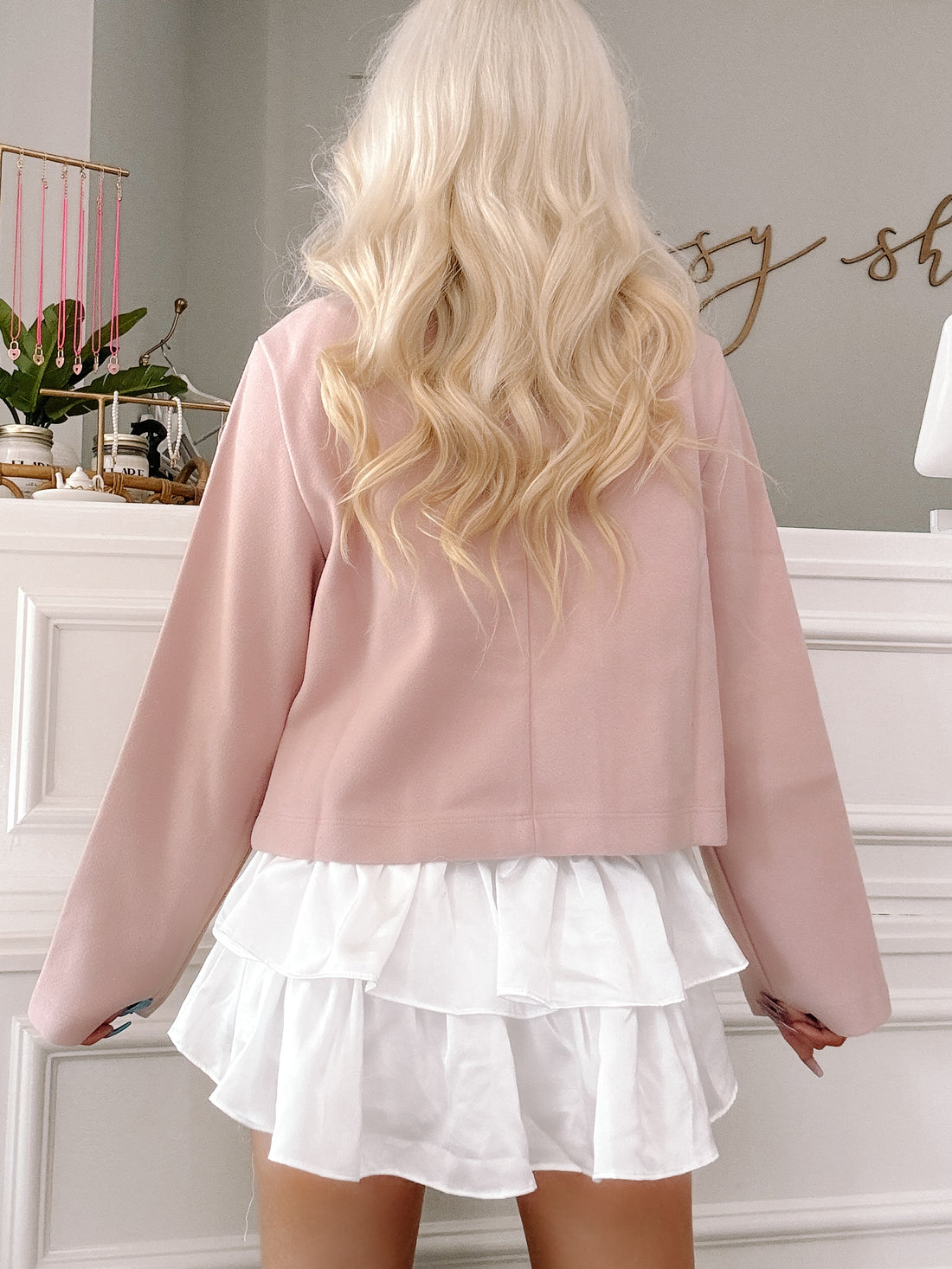 Dusty rose cropped blazer with long sleeves, shown from the back, layered over a white ruffled mini skirt.
