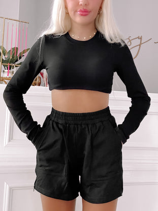 Black zip-up shorts paired with a fitted black long-sleeve top; casual wear.

