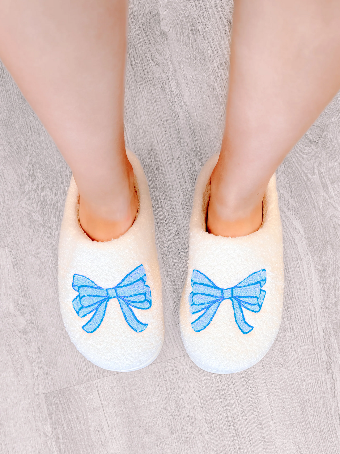 White fuzzy slippers with light blue bow embroidery for cozy comfort.
