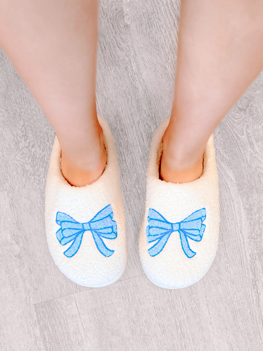 White fuzzy slippers with light blue bows, cozy and comfy for relaxing at home.
