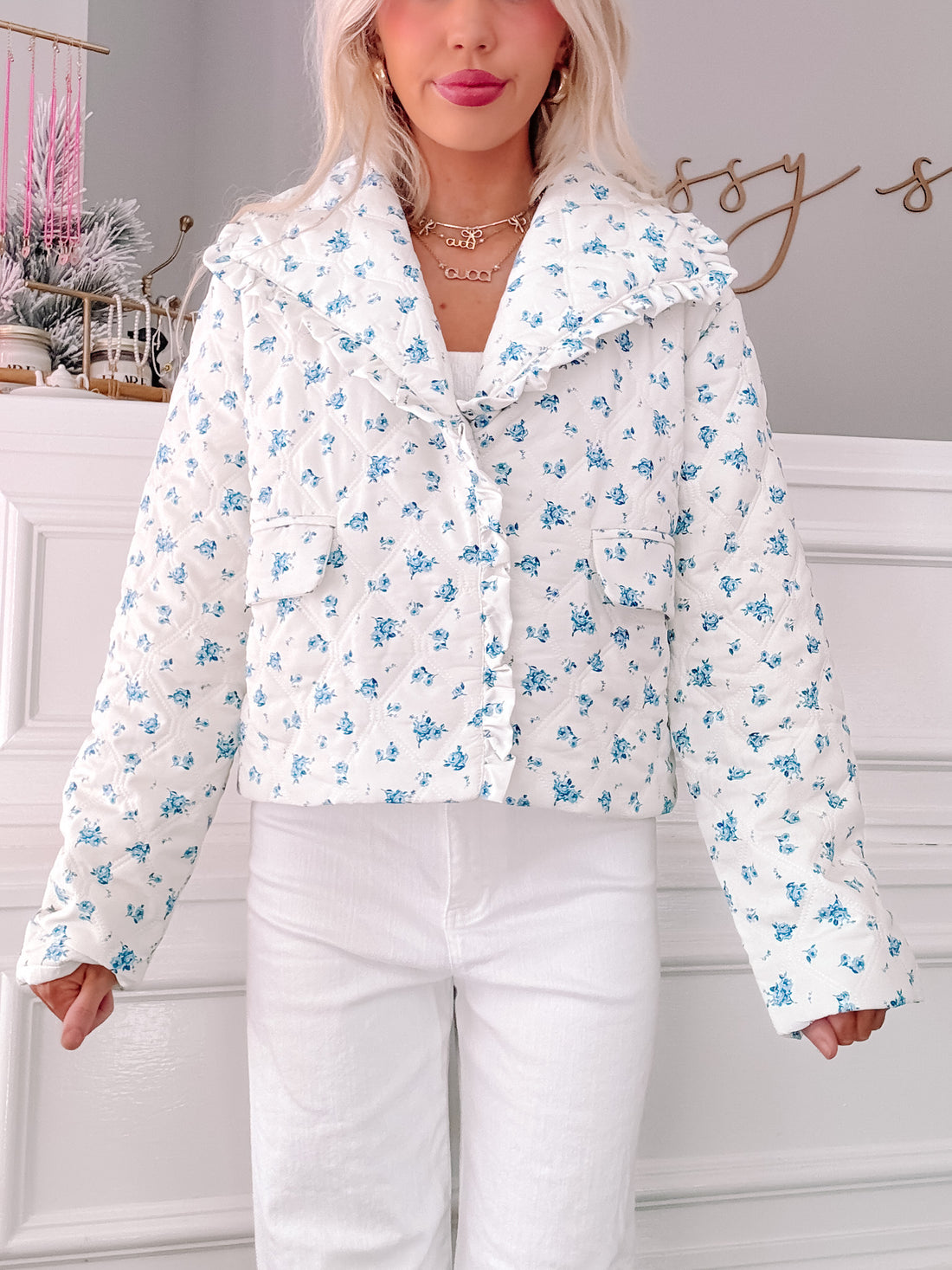 White quilted jacket with blue floral print, featuring a ruffled collar.
