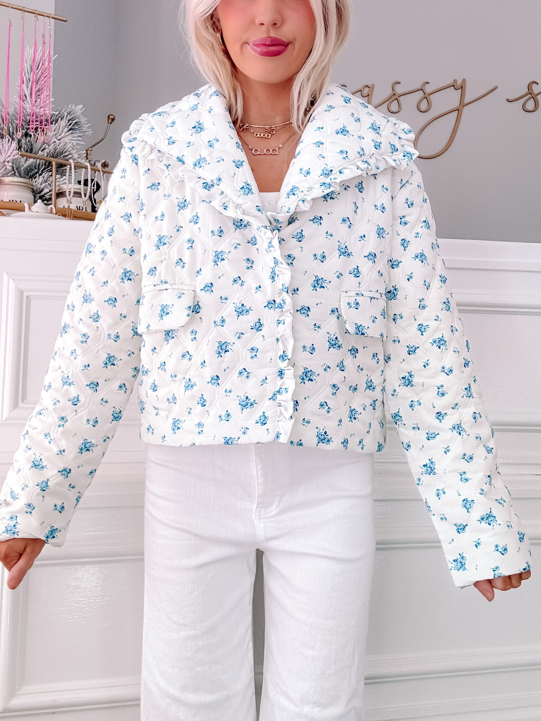 White quilted jacket with a blue floral print, featuring a ruffled collar; shown on a model.
