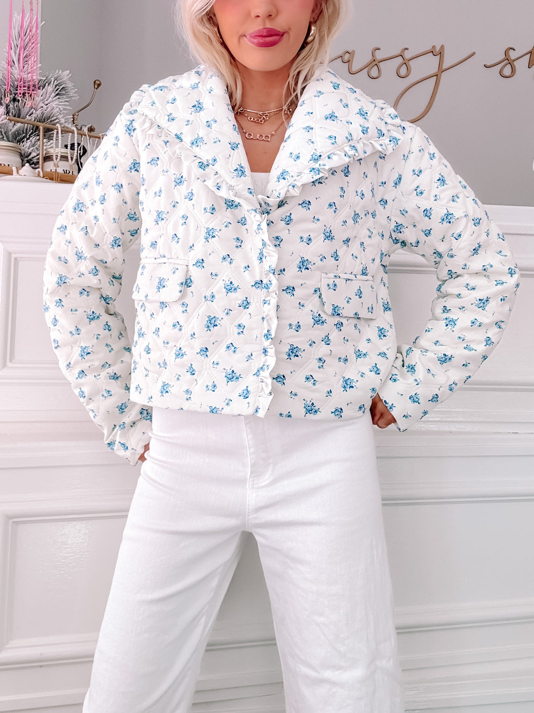 White quilted jacket with a blue floral print, ruffled collar, and front pockets.
