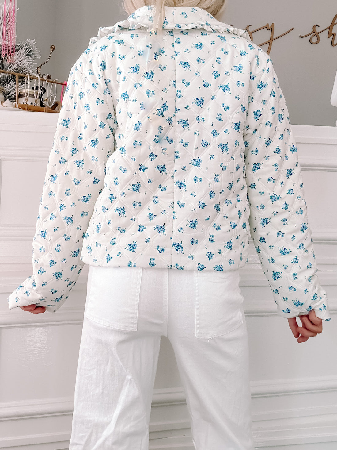 White quilted jacket with a blue floral print, shown from the back.
