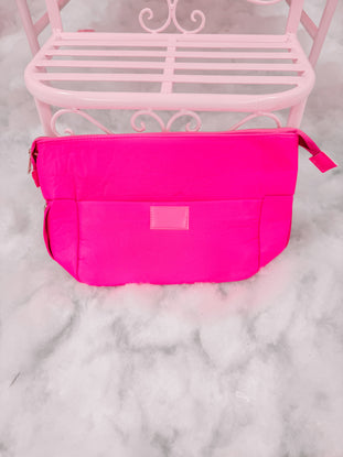 Bright neon pink zippered pouch on a pale pink metal bench.
