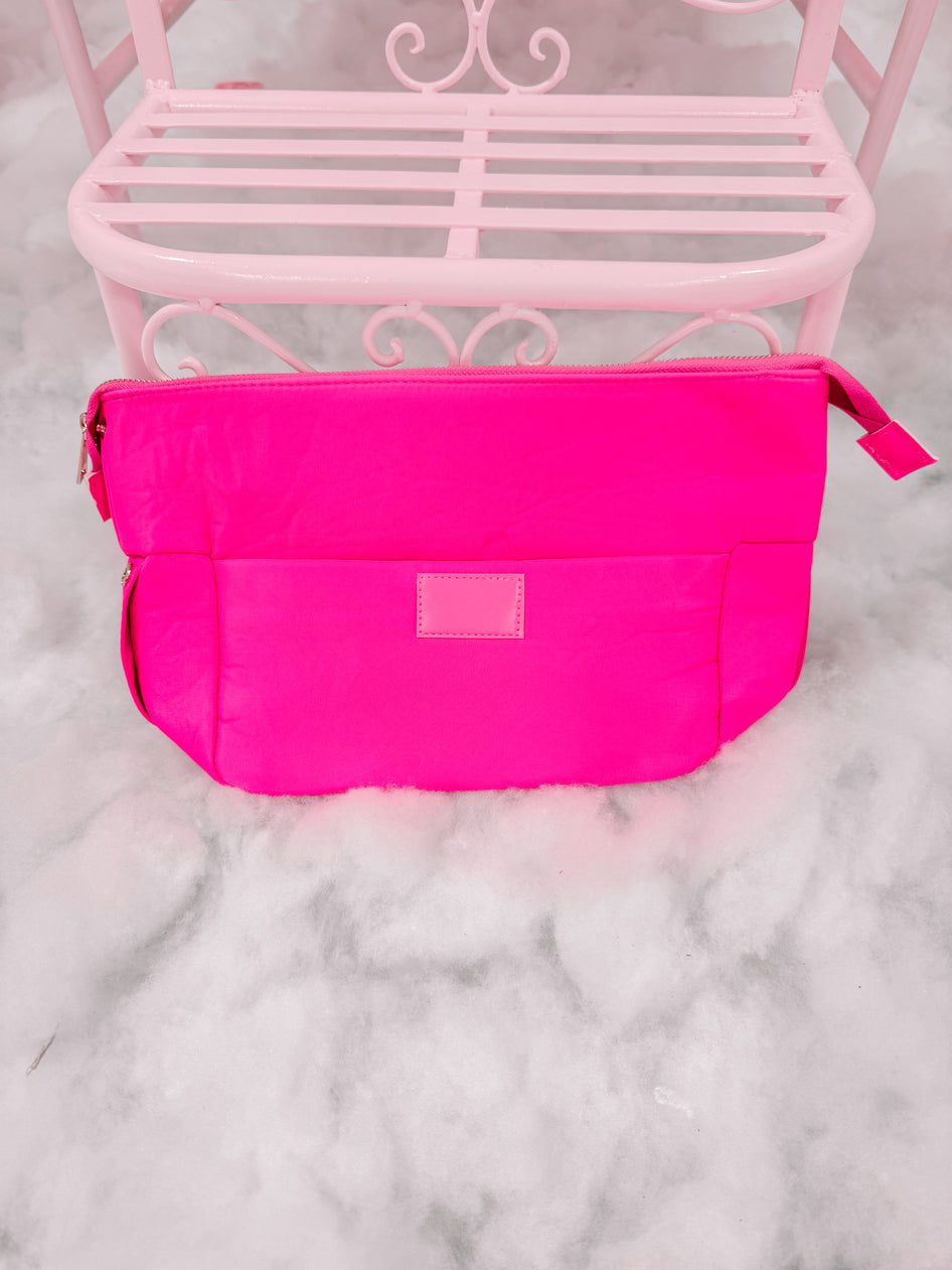Bright neon pink zippered pouch on a pale pink metal bench.
