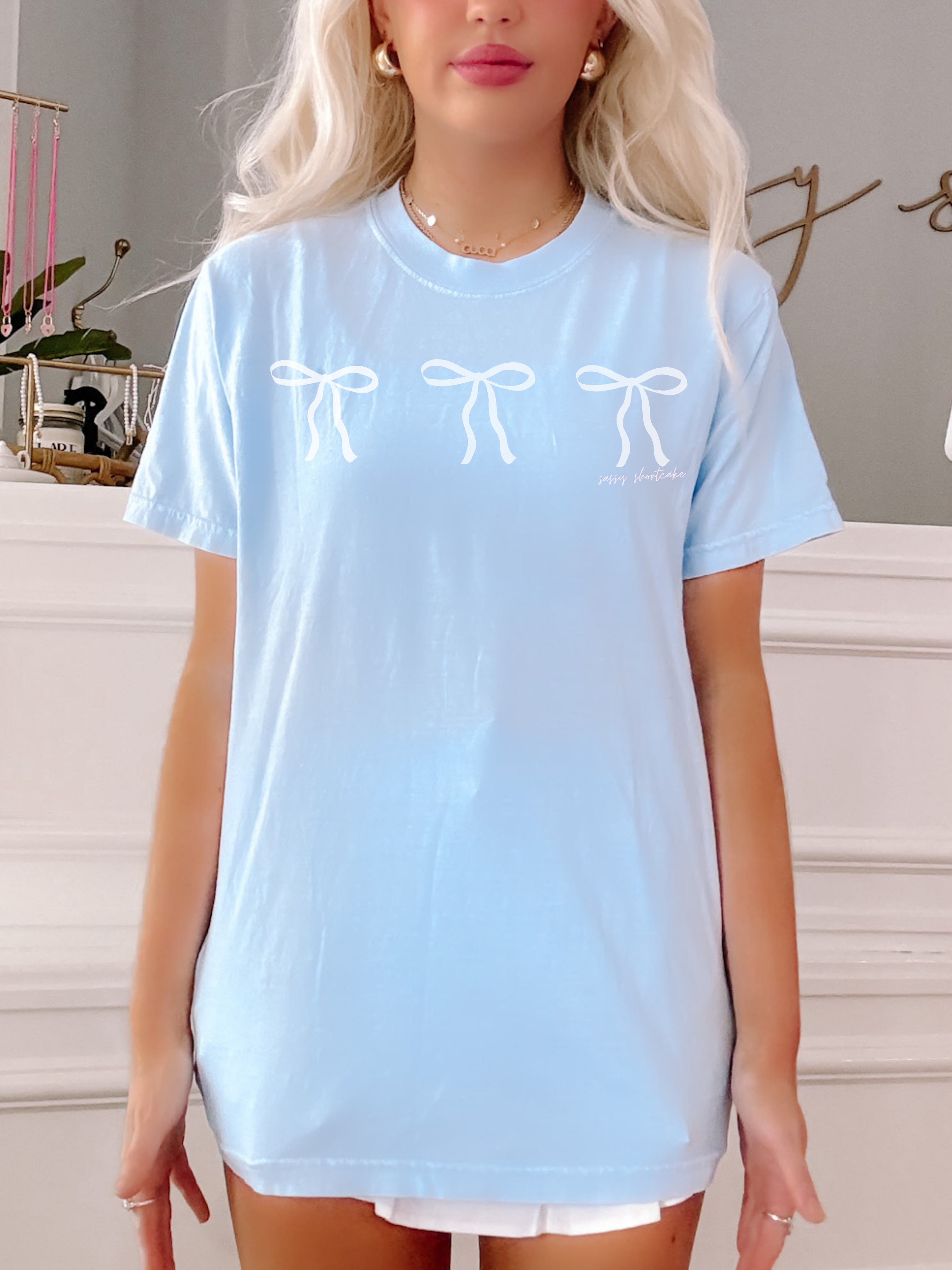 Light blue tee featuring three white bows, a casual summer style.
