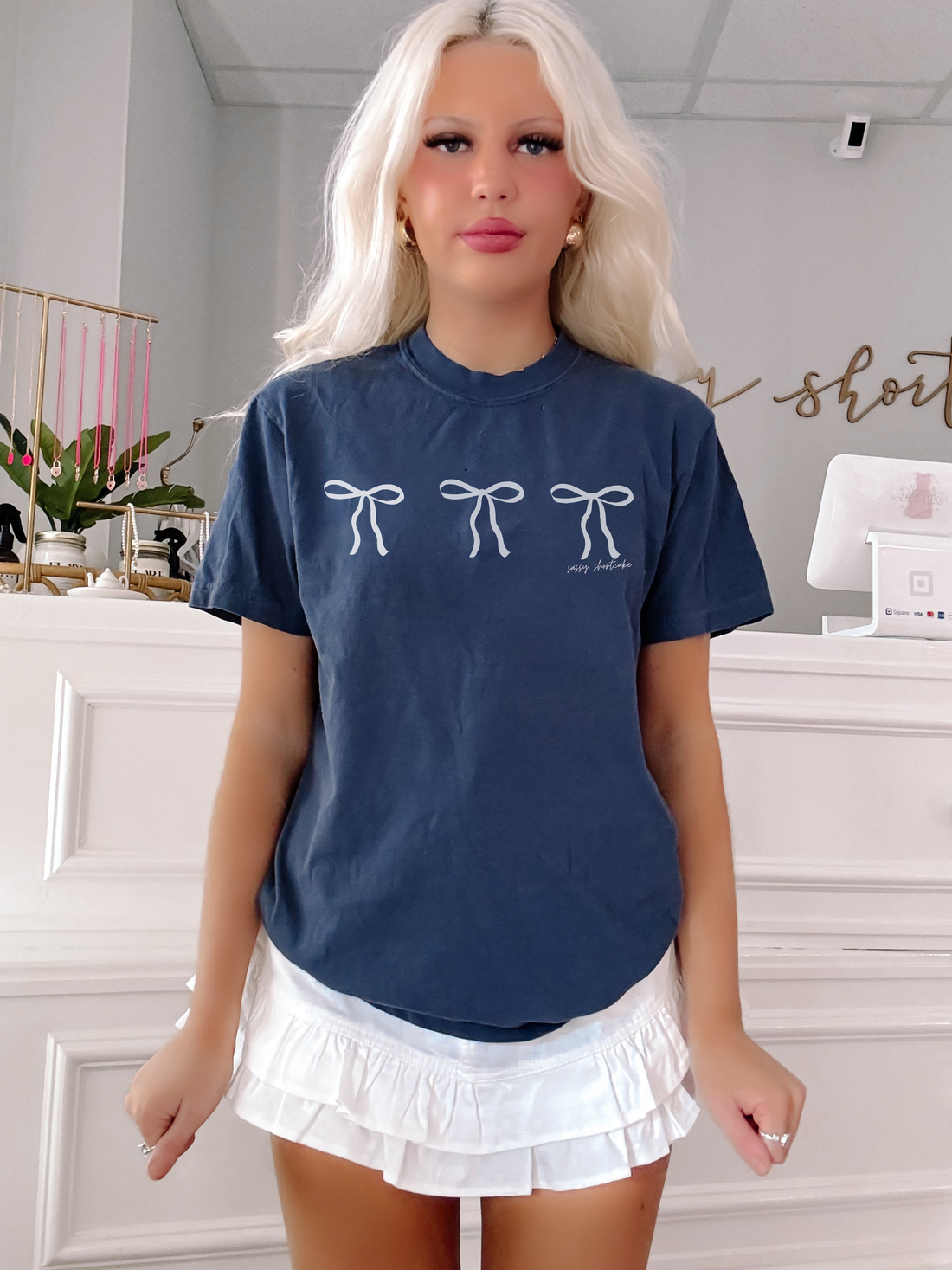 Navy blue tee featuring three white bows, modeled in a boutique.
