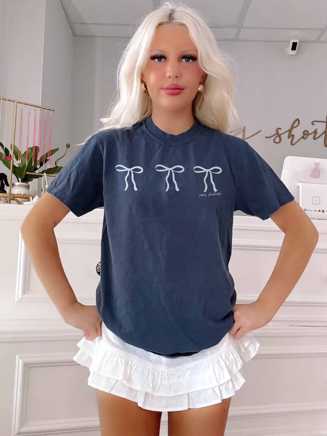 Navy blue tee shirt featuring three light grey bows, modeled against a white background.

