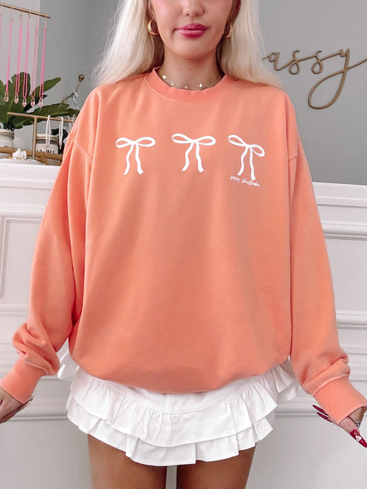 Peach crewneck sweatshirt with three white bows, styled with a white ruffled skirt.