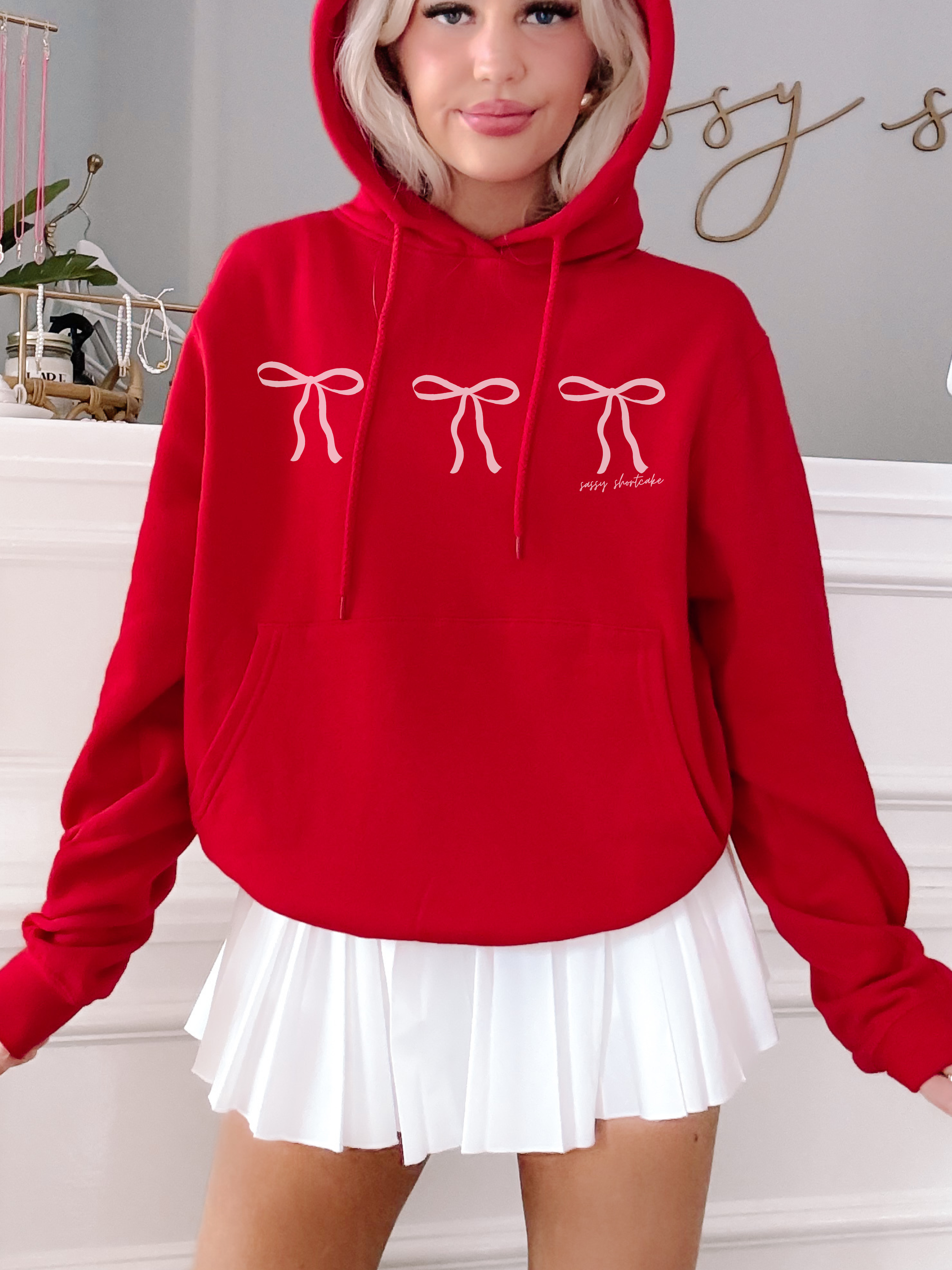 Red hoodie featuring three pink bows and the text 