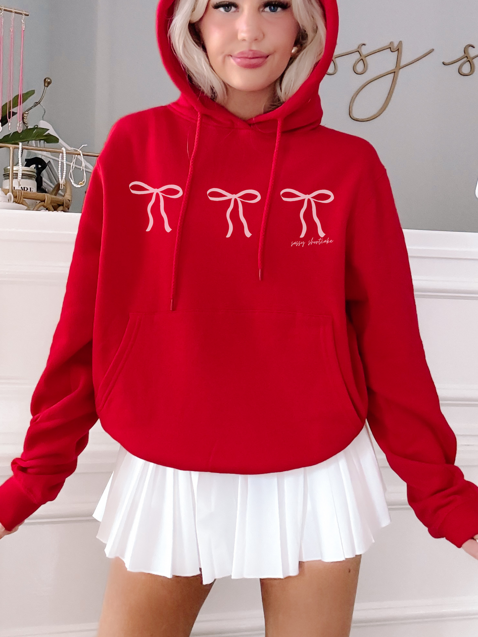 Red hoodie featuring a pink bow design, modeled with a white pleated skirt.
