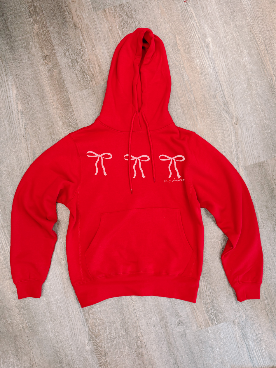 Red hoodie with pink bow print, shown on wood background.
