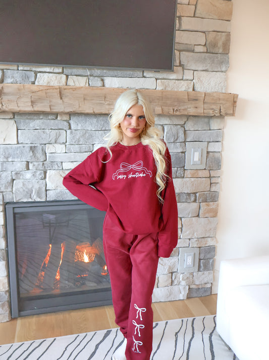 Model wearing burgundy sweatpants with an elastic waistband, pockets, and a soft micro-fleece lining, showing the three white bow design.